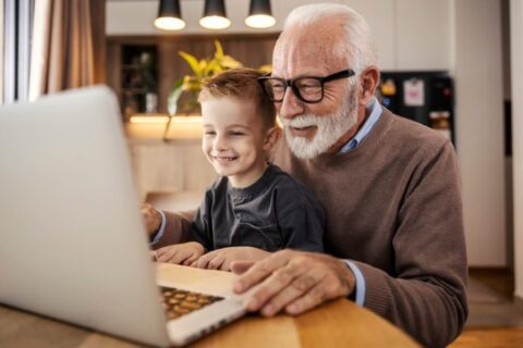 A senior and a child help each other on a laptop.