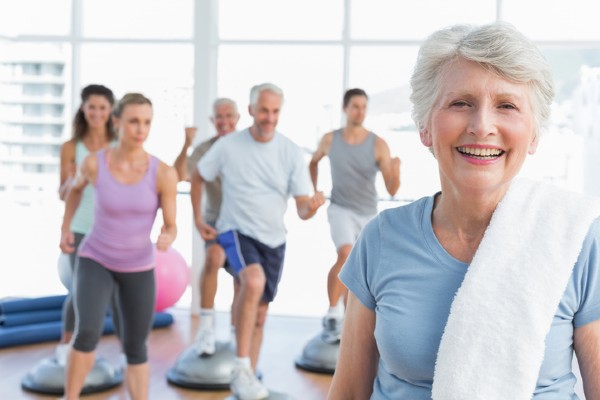 A senior woman stands in front of friends exercising in a fitness center.