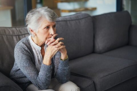 A senior woman feels stressed as she sits on a sofa.