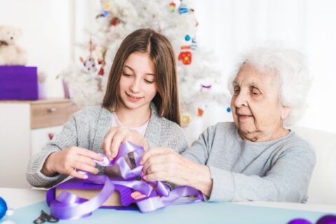 A senior woman helps her granddaughter wrap Christmas presents.