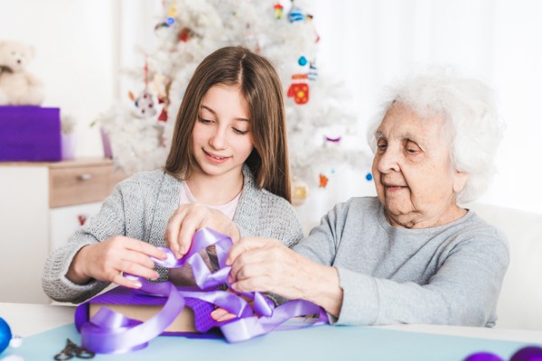 A senior woman helps her granddaughter wrap Christmas presents.