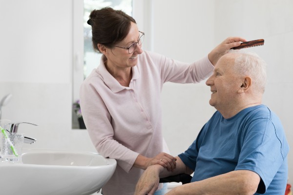 A caregiver combs the hair of a senior man.