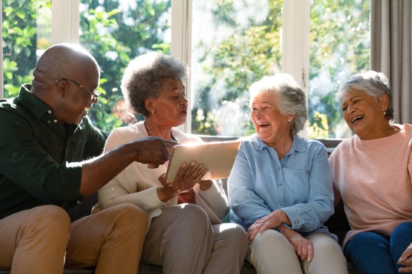 Three happy senior women and a senior man sitting on the sofa using a tablet.