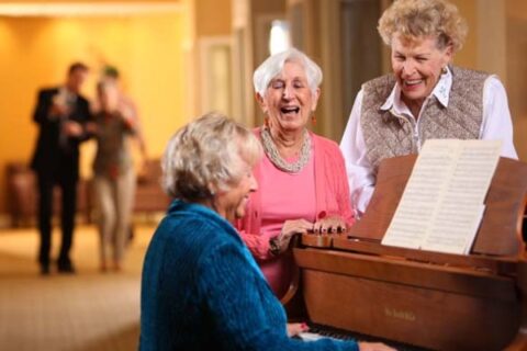 Three senior friends gather round a piano.