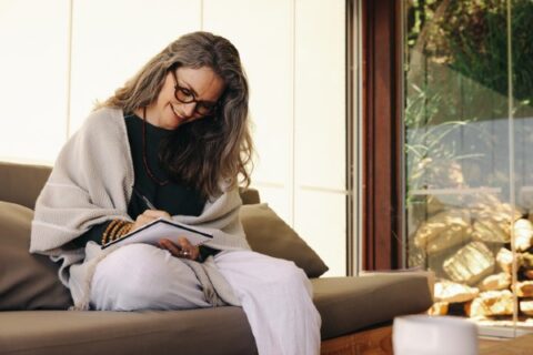 A mature woman smiling happily while writing in her journal at home.