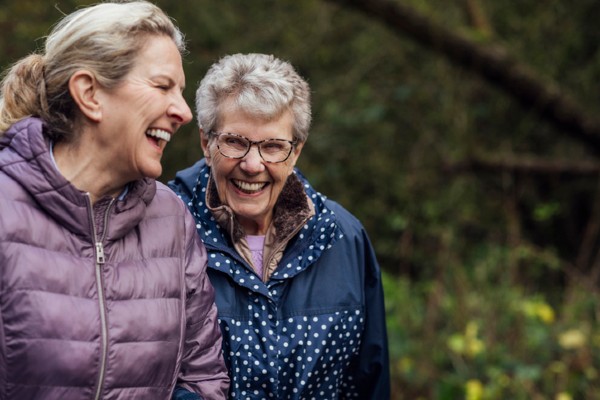 A woman walking with her senior mother through a public park while getting exercise.